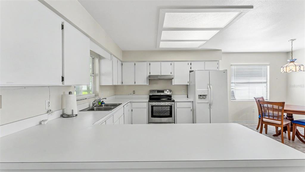 A kitchen features white cabinets, white countertops, stainless steel appliances, and an adjacent dining area — 2227 GRAND CYPRESS DRIVE, LAKELAND, FL