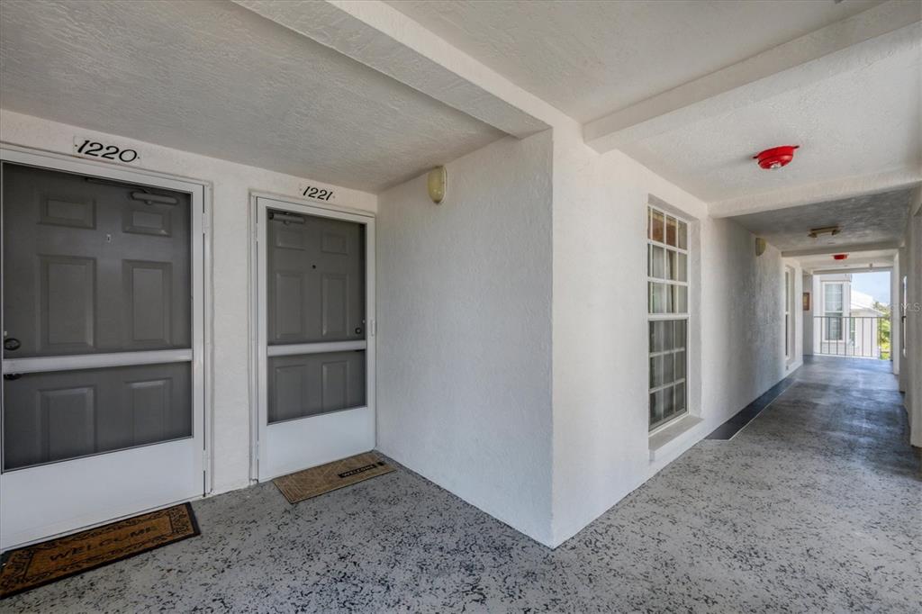 An exterior apartment hallway features two gray doors, white walls, and a concrete floor — 7070 PLACIDA ROAD UNIT 1221, PLACIDA, FL