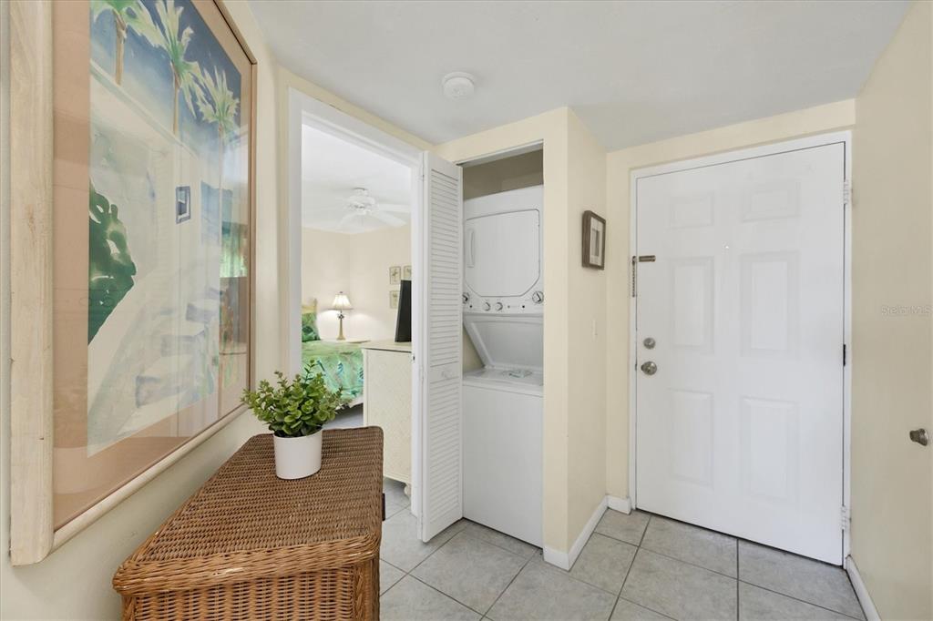 An entryway features a wicker table, a stacked washer-dryer unit, and a view into a bedroom — 7070 PLACIDA ROAD UNIT 1221, PLACIDA, FL
