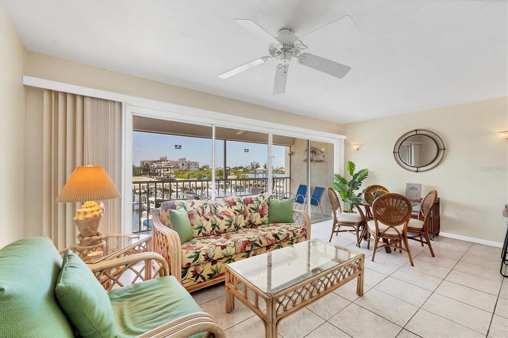 A living and dining area with rattan furniture, tile floors, and a balcony overlooking water — 7070 PLACIDA ROAD UNIT 1221, PLACIDA, FL