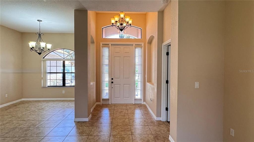 An entryway with tile flooring, a white front door, and a chandelier leads to a dining area — 406 CINNAMON DRIVE, POINCIANA, FL