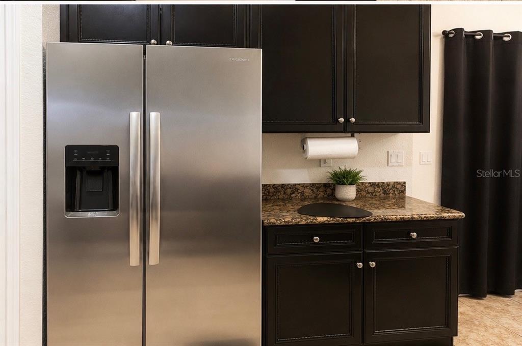 A stainless steel refrigerator stands next to dark cabinets and a granite countertop in a kitchen — 406 CINNAMON DRIVE, POINCIANA, FL
