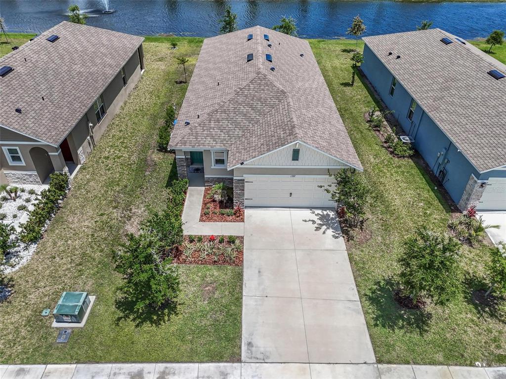 An aerial view shows a single-story house with a concrete driveway and a backyard pond — 1337 CORK DRIVE, ORMOND BEACH, FL