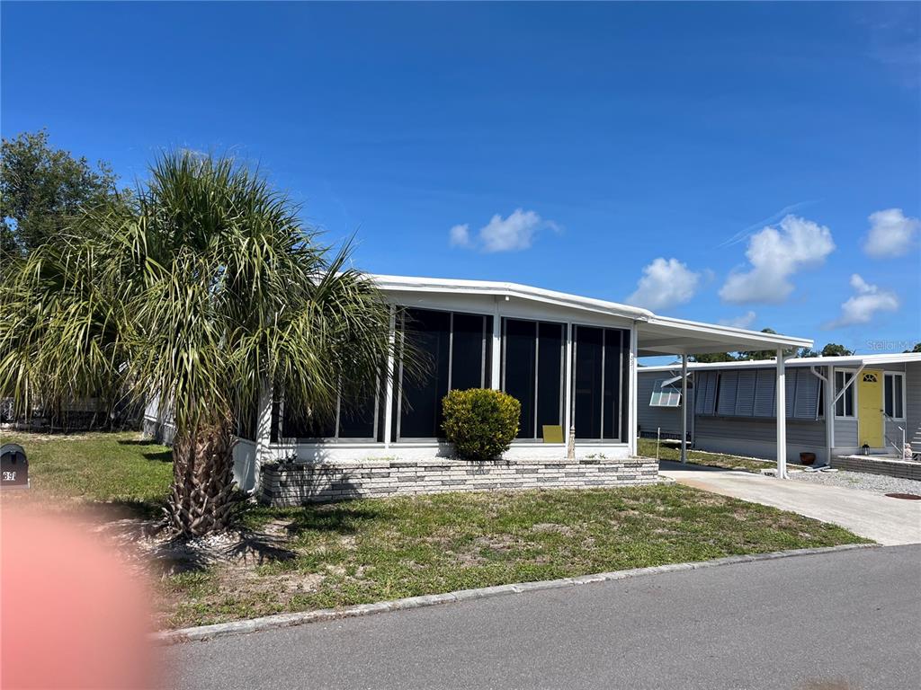 A single-story mobile home with a screened-in porch, a carport, and a palm tree — 891 GRADO DRIVE, VENICE, FL