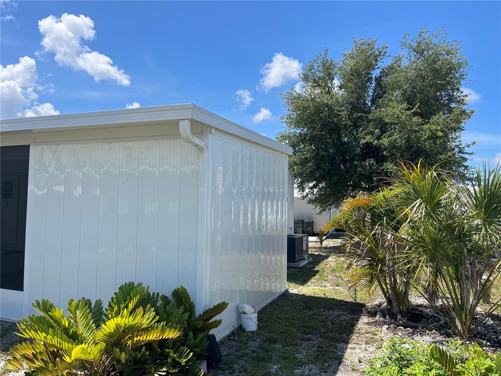 The exterior of a white mobile home features a metal wall, gutter, and landscaping — 891 GRADO DRIVE, VENICE, FL