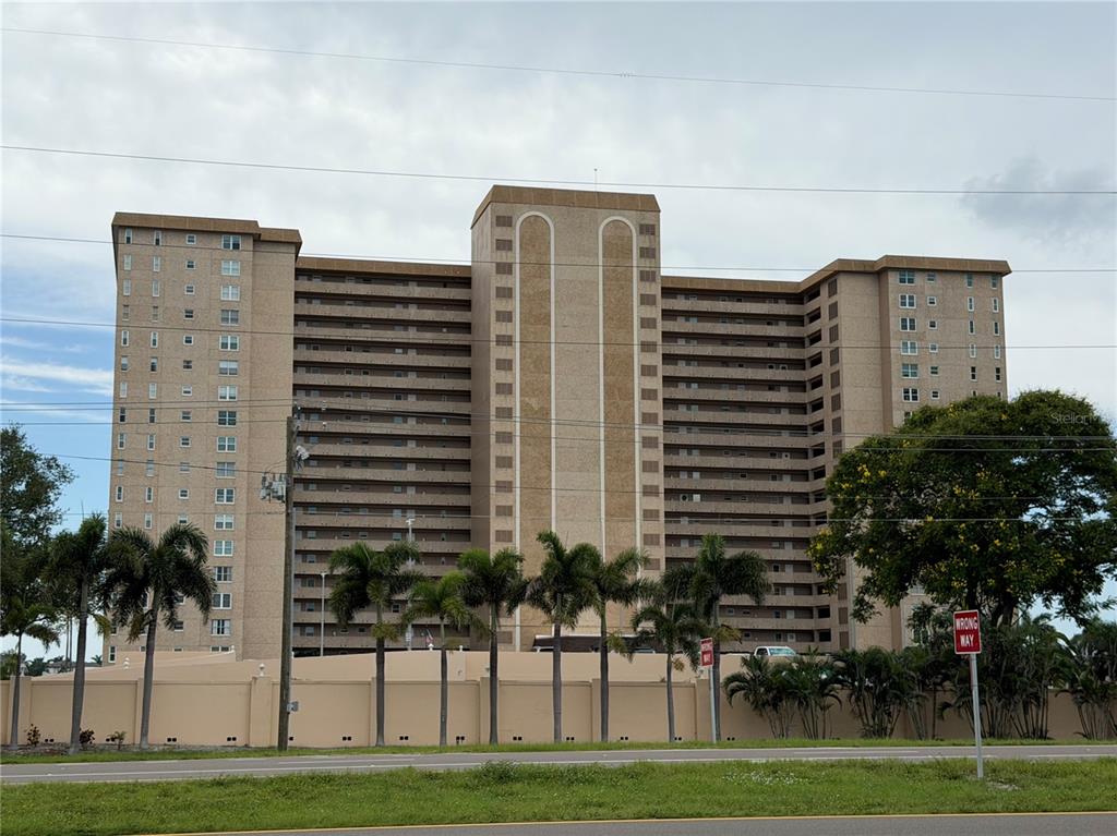 A tall, multi-story tan apartment building stands behind a row of palm trees and a wall — 5200 BRITTANY DRIVE S UNIT 609, ST PETERSBURG, FL