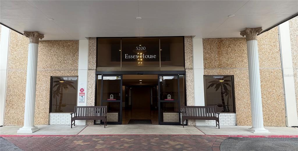 The exterior entrance of a building features two white columns, glass doors, and wooden benches — 5200 BRITTANY DRIVE S UNIT 609, ST PETERSBURG, FL