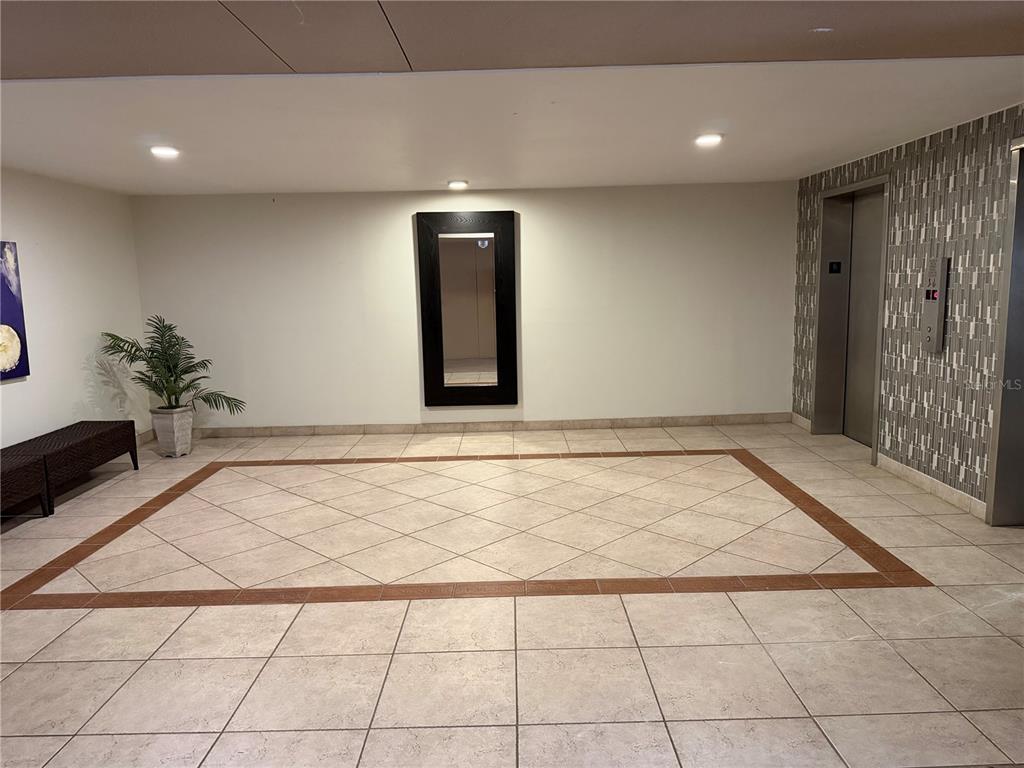 A tiled elevator lobby features a dark-framed mirror, a bench, and a potted plant — 5200 BRITTANY DRIVE S UNIT 609, ST PETERSBURG, FL