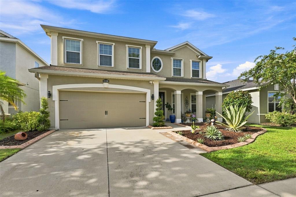 A two-story suburban house with a beige stucco exterior, a two-car garage, and landscaping — 11156 SPRING POINT CIRCLE, RIVERVIEW, FL