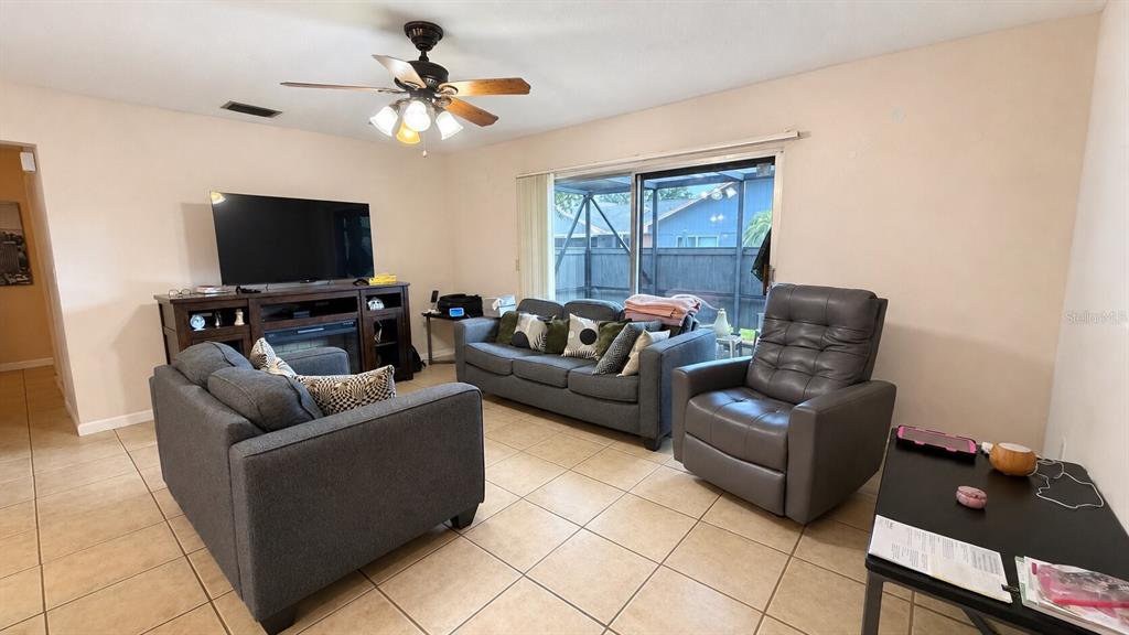 A living room features tile flooring, a ceiling fan, a television console, and gray furniture — 3914 NW CINNAMON TREE CIRCLE, JENSEN BEACH, FL
