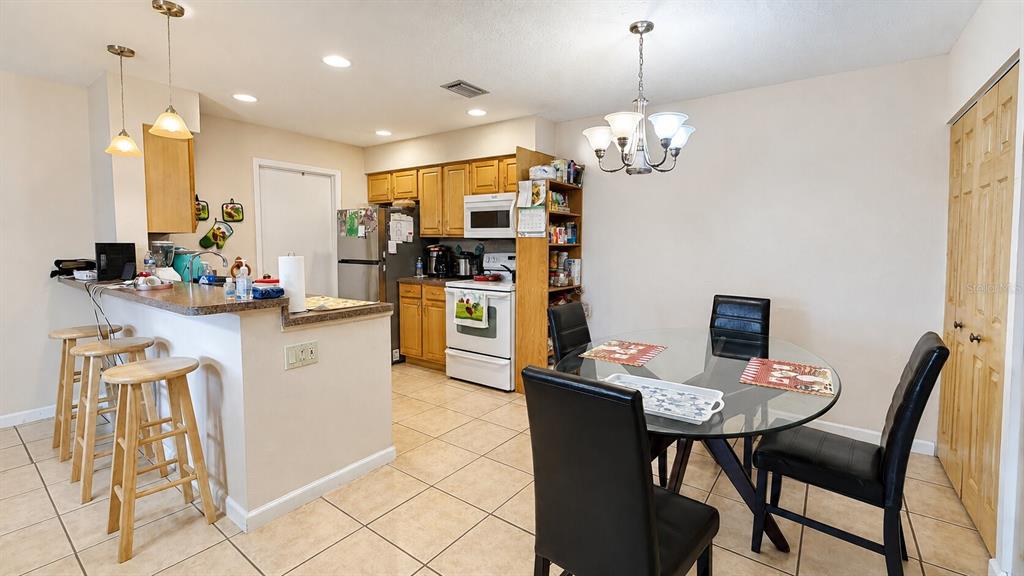 A kitchen with light wood cabinets and a dining area with a glass table — 3914 NW CINNAMON TREE CIRCLE, JENSEN BEACH, FL