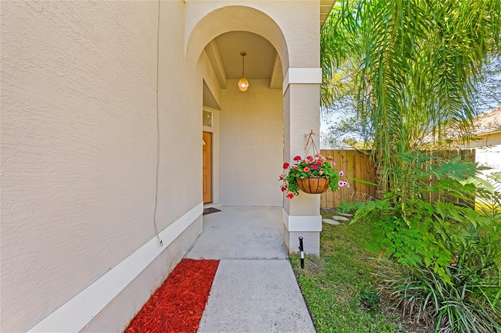 A covered entryway features a concrete walkway, an arched ceiling, and a hanging flower basket — 408 LANCERS DRIVE, WINTER SPRINGS, FL