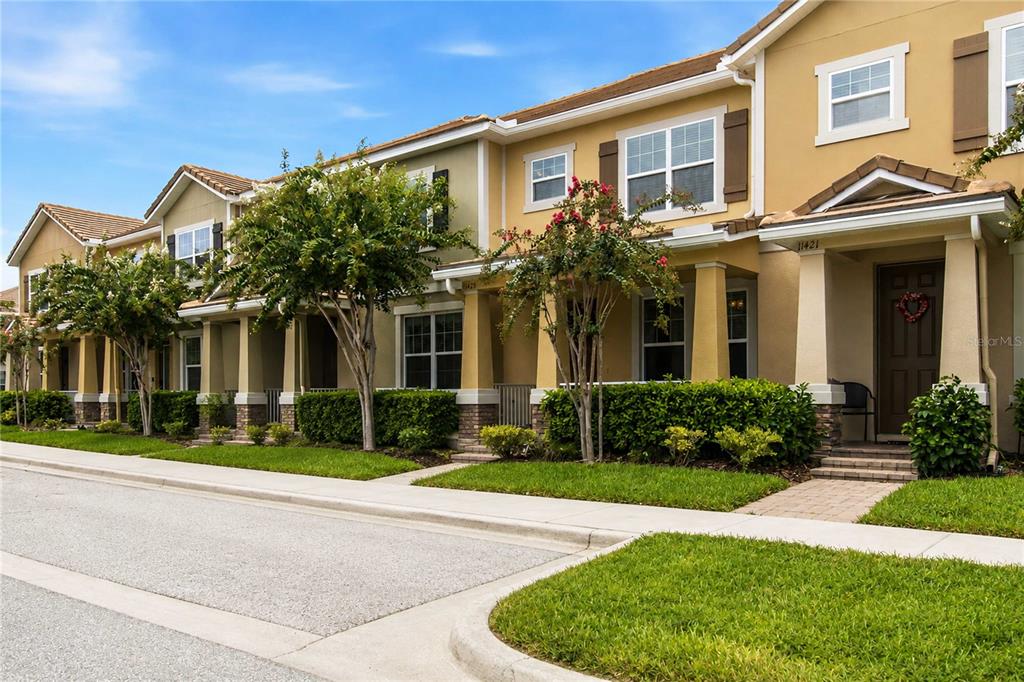 A row of two-story townhomes with tan stucco siding, brown shutters, and small front porches — 11425 BROWNSTONE STREET, WINDERMERE, FL