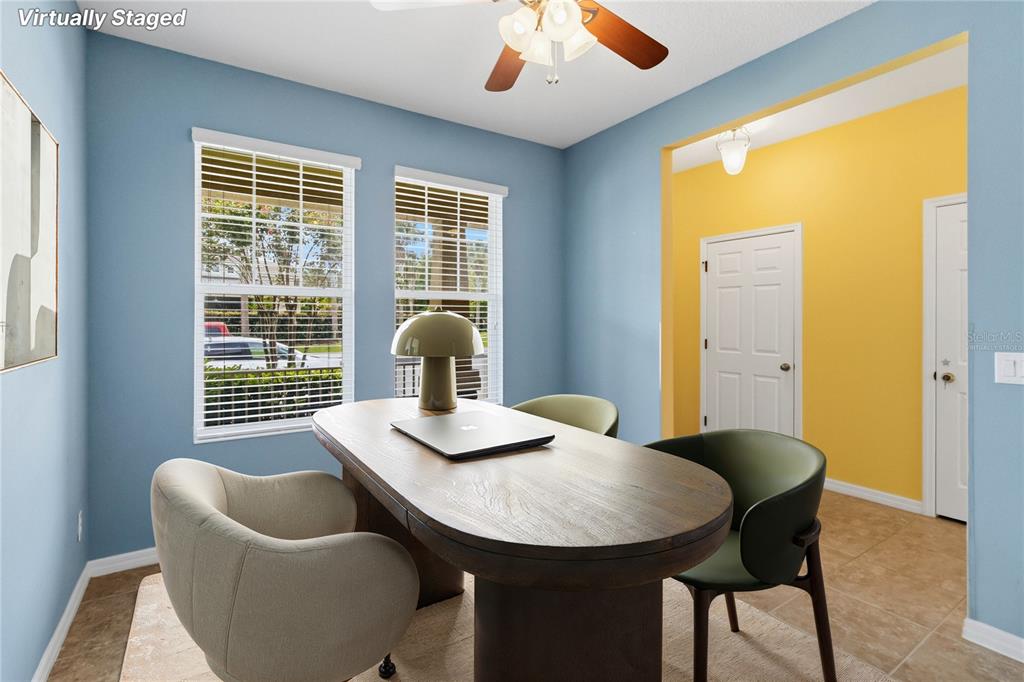 A virtually staged home office features blue walls, a wooden desk, and two windows — 11425 BROWNSTONE STREET, WINDERMERE, FL