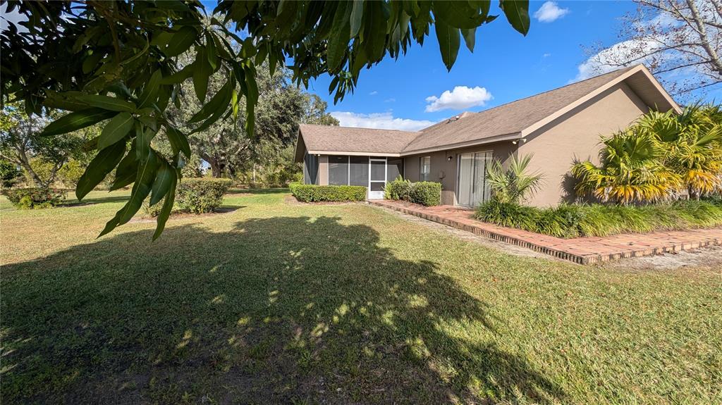 A tan house with a screened-in porch and a brick patio sits on a lawn — 408 LEXINGTON DRIVE, SEBRING, FL