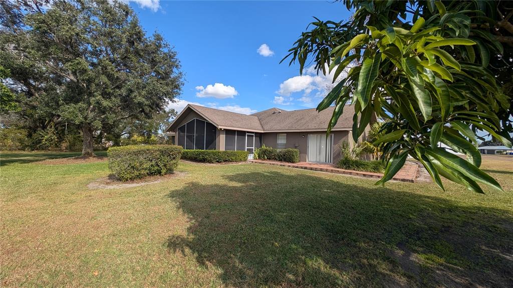 The exterior of a single-story house features a screened-in porch, a brick patio, and landscaping — 408 LEXINGTON DRIVE, SEBRING, FL