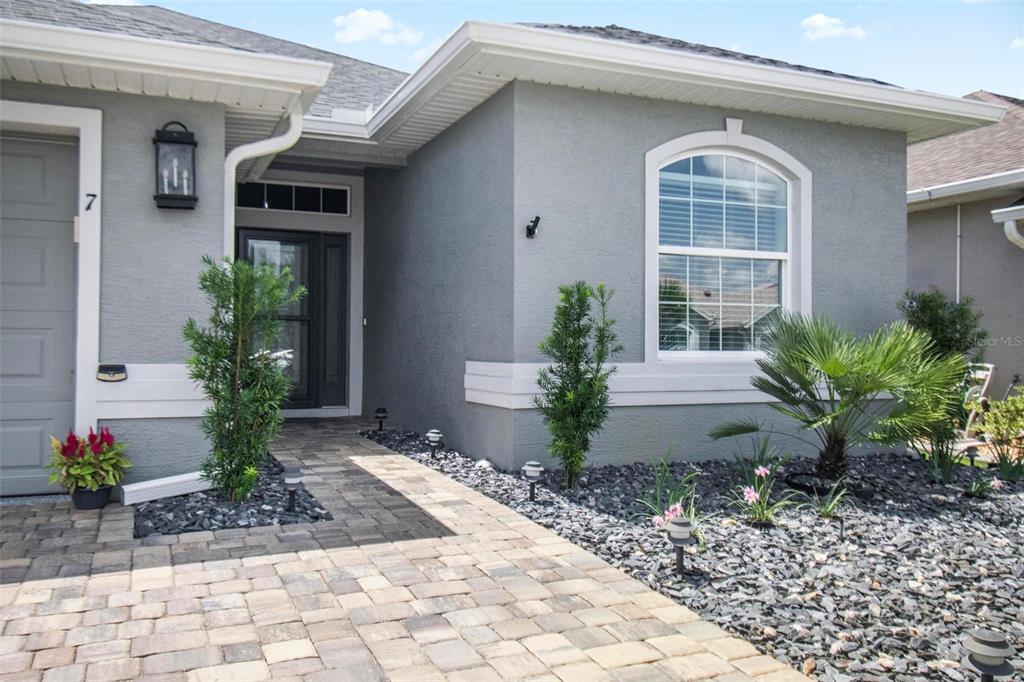 A gray house exterior features a stone paver walkway, dark landscaping rocks, and a front door — 7 TIDEWAY TRAIL, PALM COAST, FL