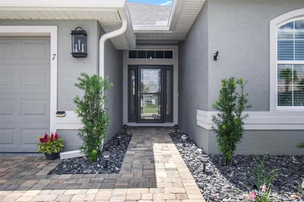 A paved walkway leads to the front entrance of a gray house with two small trees — 7 TIDEWAY TRAIL, PALM COAST, FL