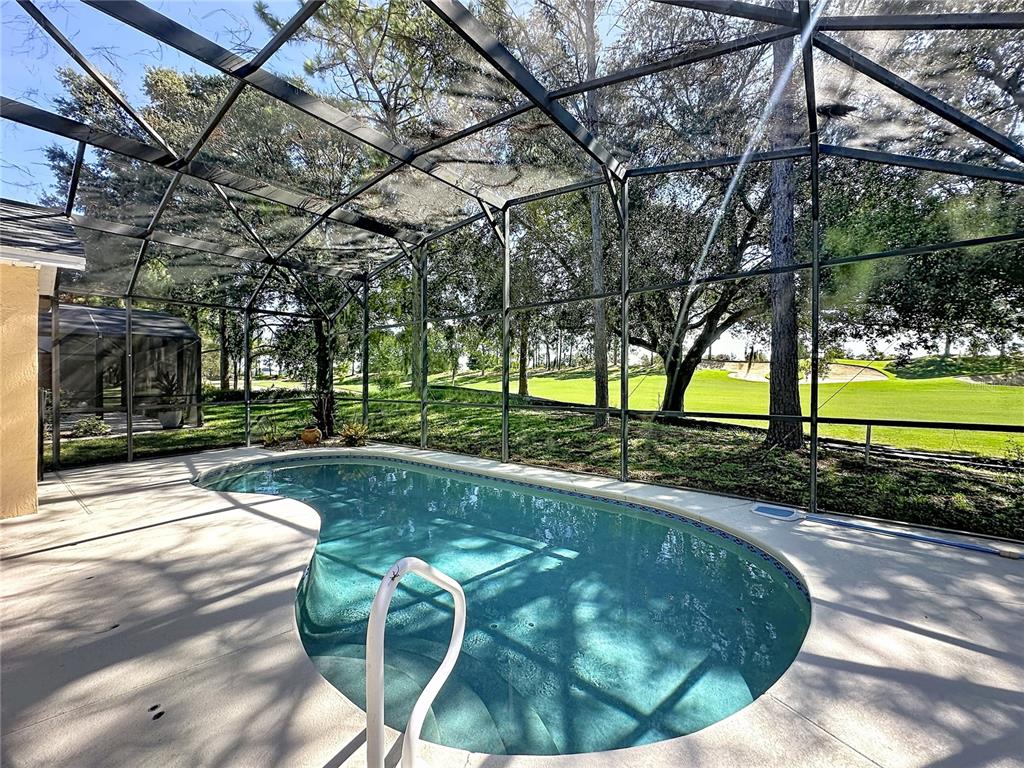 A screened-in swimming pool overlooks a golf course with mature trees in the background — 2817 KOKOMO LOOP, HAINES CITY, FL
