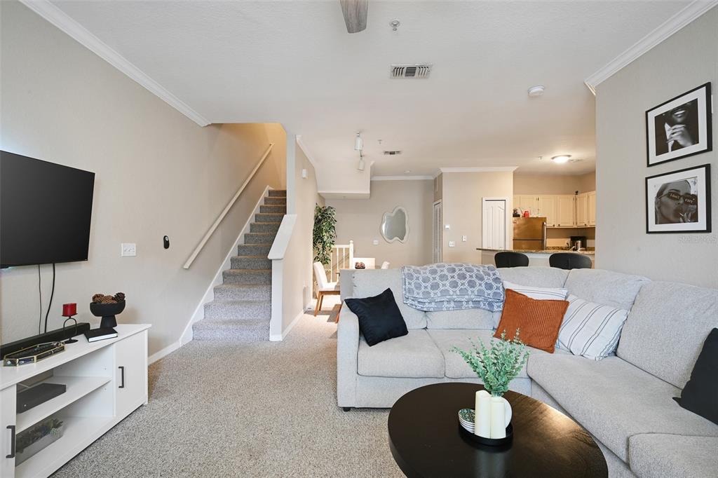 A living room features a sectional sofa, a television, stairs, and an open kitchen area — 2637 LEGACY VILLAS DRIVE UNIT 2637, MAITLAND, FL