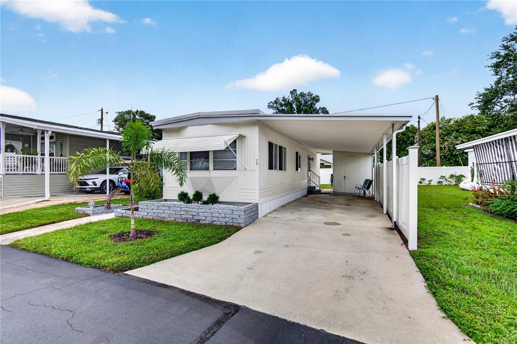 A single-story mobile home with a concrete driveway, carport, and a small front garden — 9900 ULMERTON ROAD UNIT 28, LARGO, FL