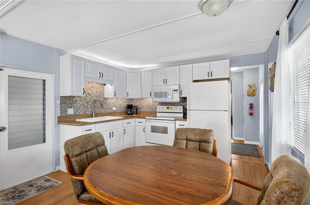 A kitchen features white cabinets, a mosaic tile backsplash, and a round wooden dining table — 9900 ULMERTON ROAD UNIT 28, LARGO, FL