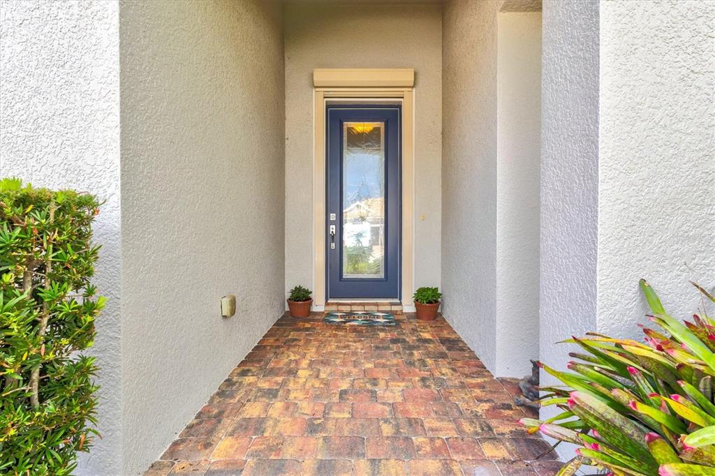 A single-story house exterior features a blue garage, a front entryway, and landscaped garden beds — 19556 PETRINO STREET, VENICE, FL