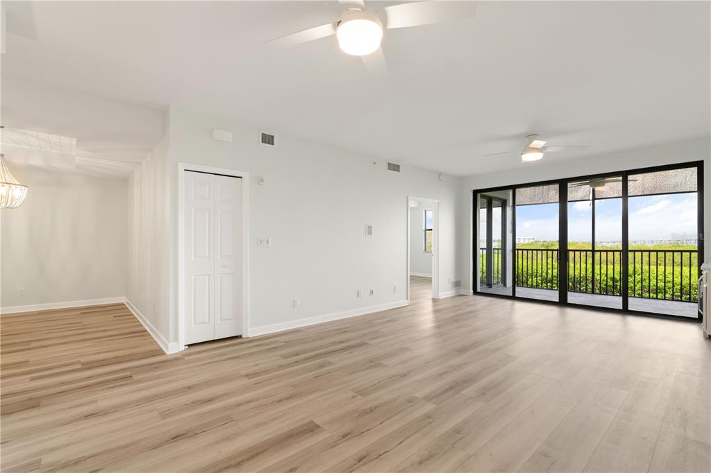 A bright living room features light wood-look flooring, a ceiling fan, and sliding glass balcony doors — 900 E MARION AVENUE UNIT 1203, PUNTA GORDA, FL