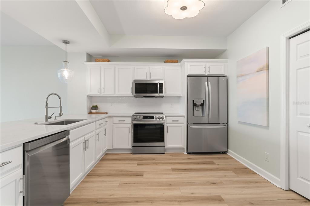 A modern kitchen features white cabinets, stainless steel appliances, and light wood-look flooring — 900 E MARION AVENUE UNIT 1203, PUNTA GORDA, FL