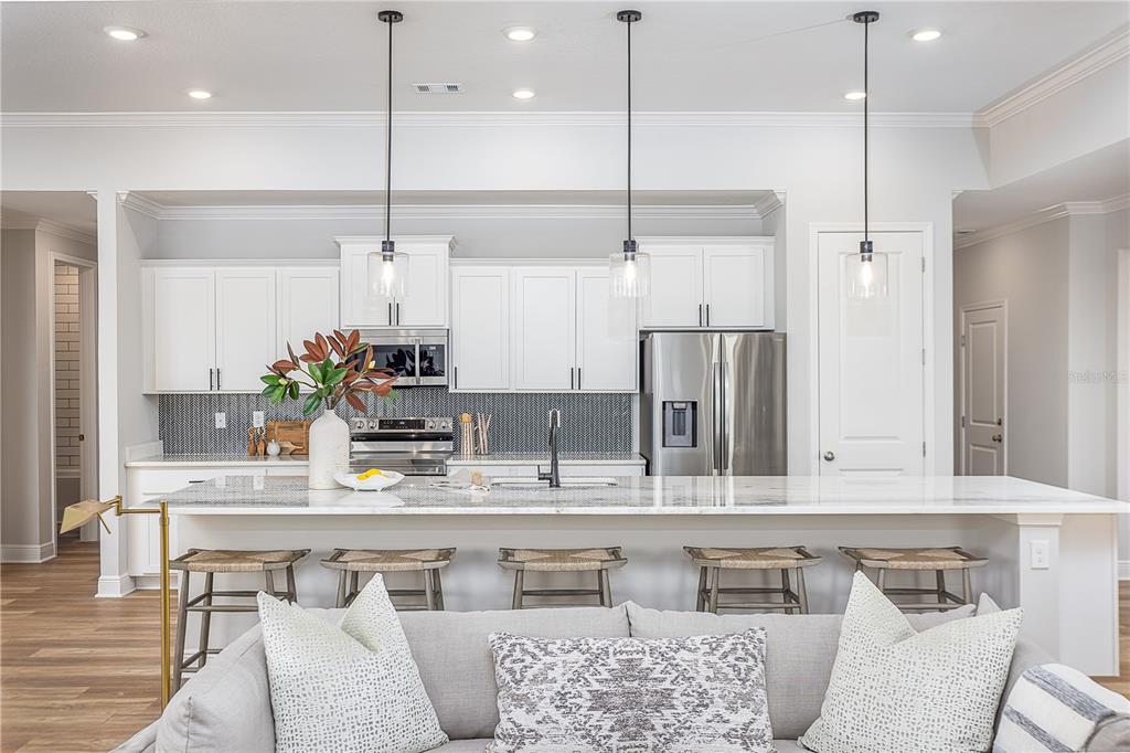 A modern kitchen features white cabinetry, a marble island with bar seating, and stainless appliances — 52 CACTUS STREET E, HOMOSASSA, FL