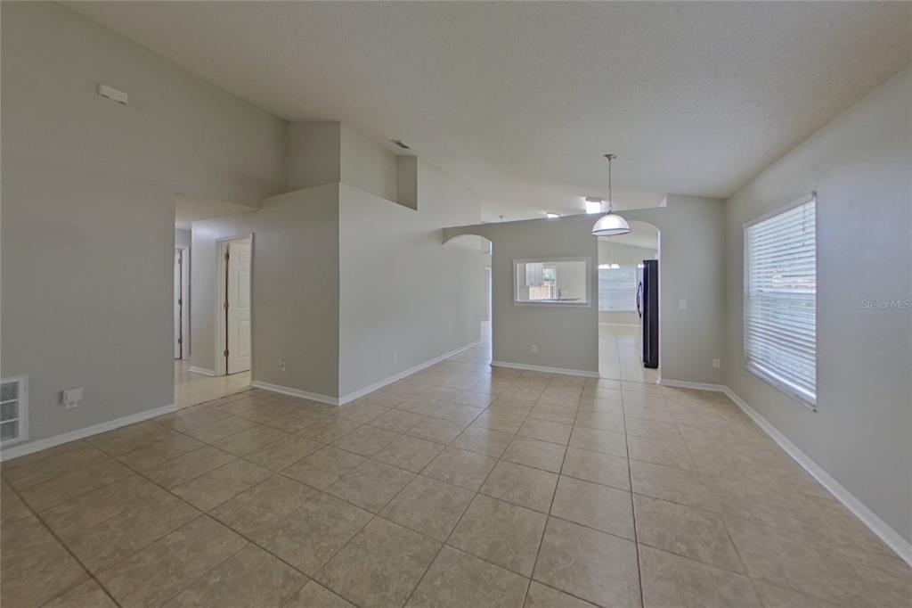 An open-concept living area features light-colored tile flooring, vaulted ceilings, and a pass-through kitchen window — 13809 RIVERPATH GROVE DRIVE, ORLANDO, FL
