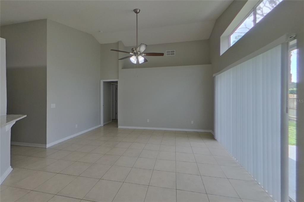 An empty living room features light-colored tile flooring, a ceiling fan, and large sliding glass doors — 13809 RIVERPATH GROVE DRIVE, ORLANDO, FL