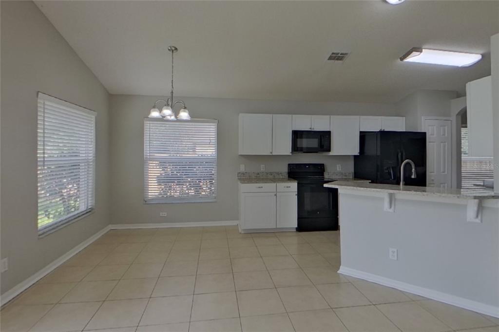 A kitchen and dining area with white cabinets, black appliances, and light-colored tile flooring — 13809 RIVERPATH GROVE DRIVE, ORLANDO, FL