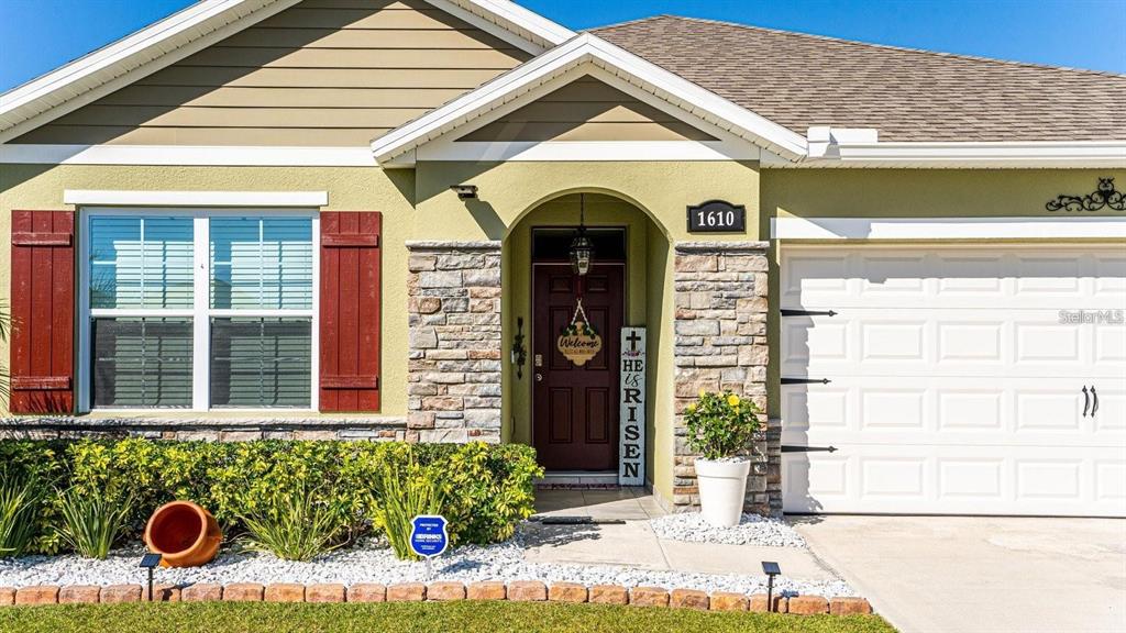 A single-story house exterior features a stone-accented entryway, a white garage door, and red shutters — 1610 SPRAY TERRACE, ST CLOUD, FL