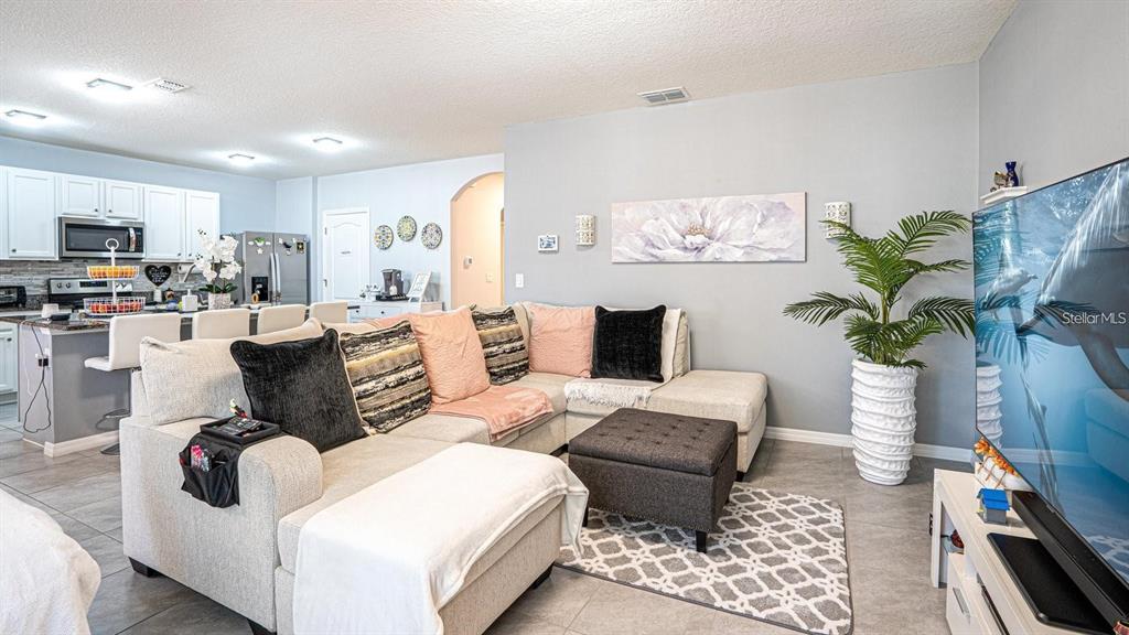 A living room with a sectional sofa, ottoman, and television opens to a kitchen area — 1610 SPRAY TERRACE, ST CLOUD, FL
