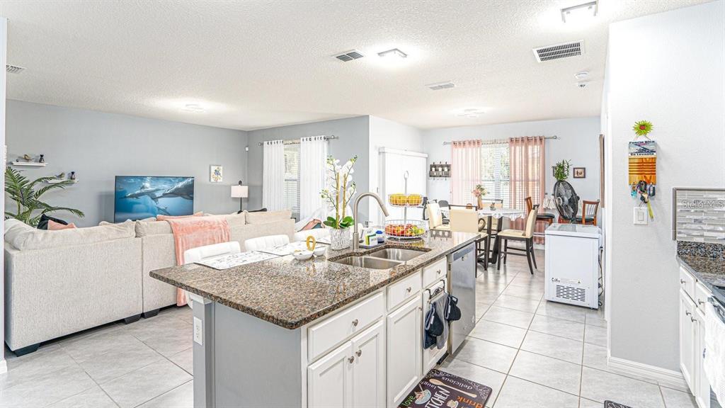 An open-concept kitchen with a granite island overlooks a living room and dining area — 1610 SPRAY TERRACE, ST CLOUD, FL