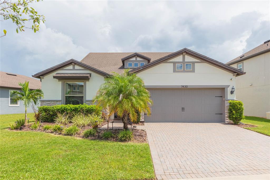 A single-story house with a beige stucco exterior, stone accents, and a paved driveway — 7430 POOL COMPASS LOOP, WESLEY CHAPEL, FL