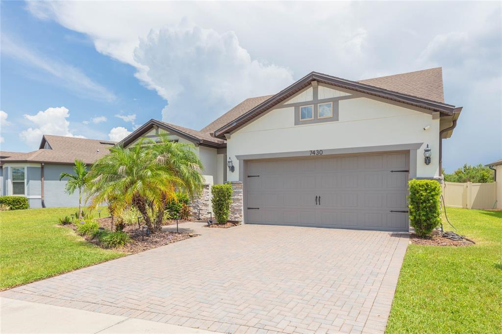A single-story house with a paved driveway, a two-car garage, and a palm tree — 7430 POOL COMPASS LOOP, WESLEY CHAPEL, FL