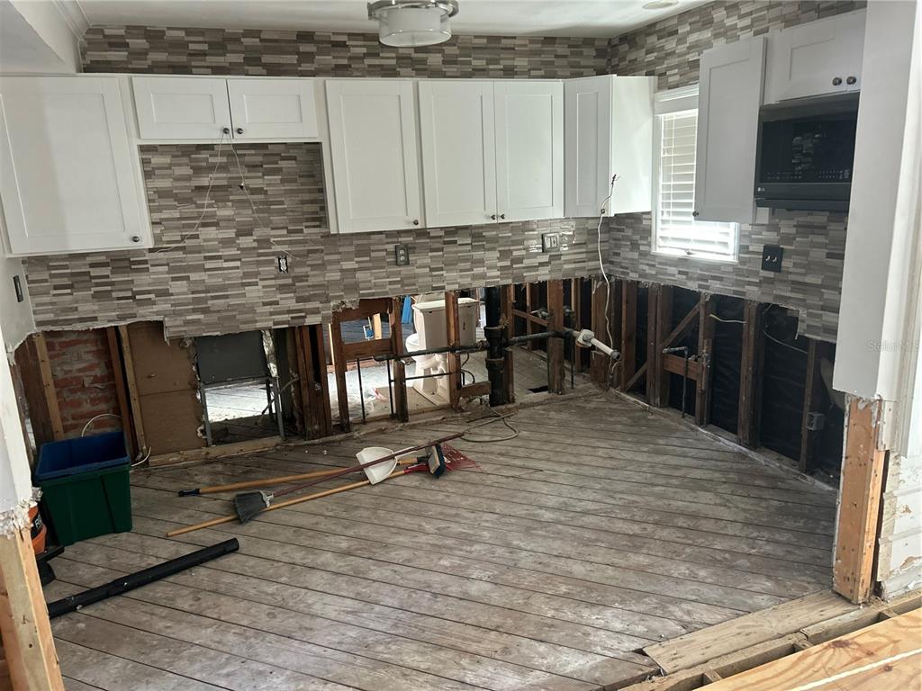 A kitchen under renovation features exposed wall studs, unfinished flooring, and installed white upper cabinets — 3008 DUPONT STREET S, GULFPORT, FL