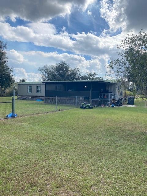 A manufactured home with a large covered porch sits on a grassy, fenced lot — 10102 LOETSCHER LANE, LITHIA, FL