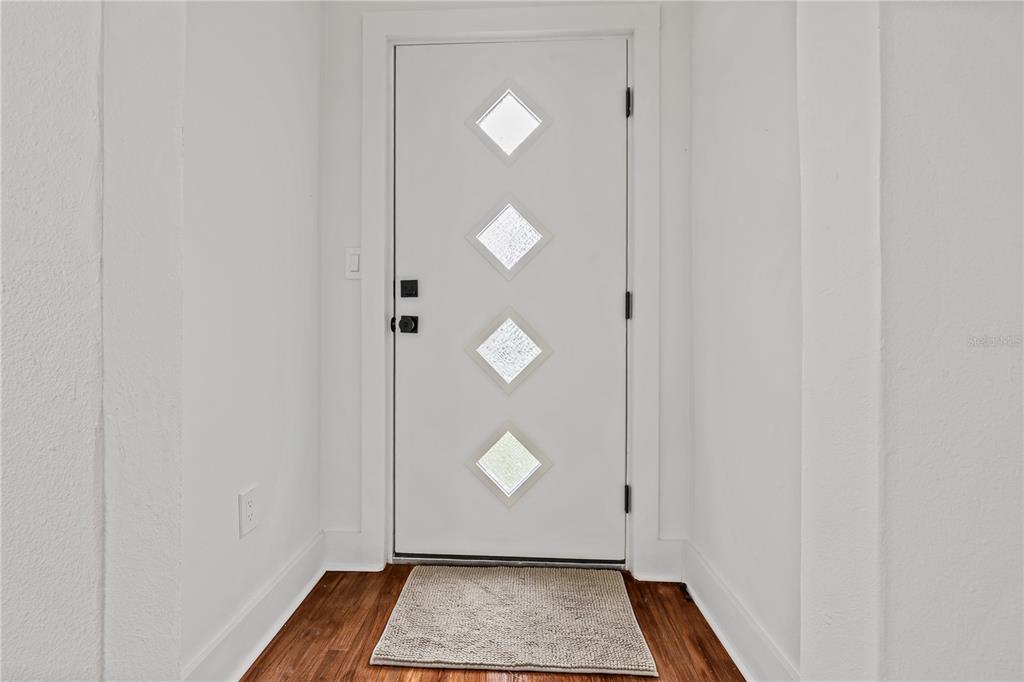 A white front door with four diamond-shaped windows sits in a hallway with wood flooring — 2202 N GLEN AVENUE, TAMPA, FL
