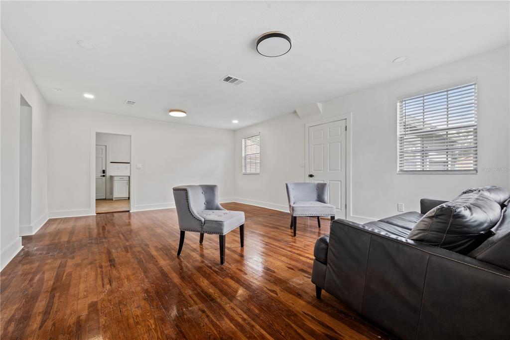 A living room with hardwood floors, white walls, two gray chairs, and a leather sofa — 2202 N GLEN AVENUE, TAMPA, FL