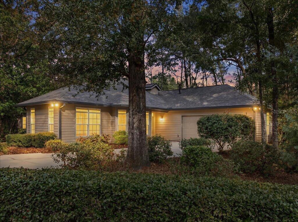 A single-story house with tan siding and a garage sits behind trees at dusk — 4412 SW 101ST DRIVE, GAINESVILLE, FL