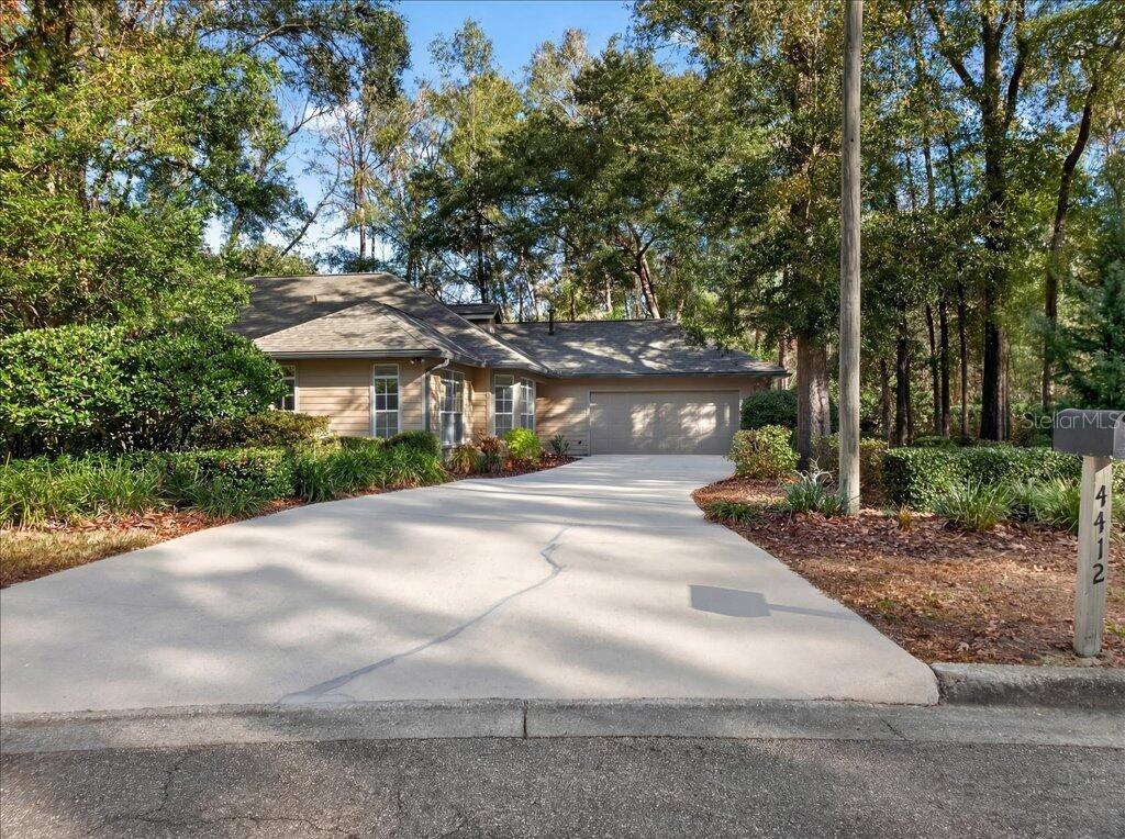 A tan house with a concrete driveway sits in a wooded lot — 4412 SW 101ST DRIVE, GAINESVILLE, FL