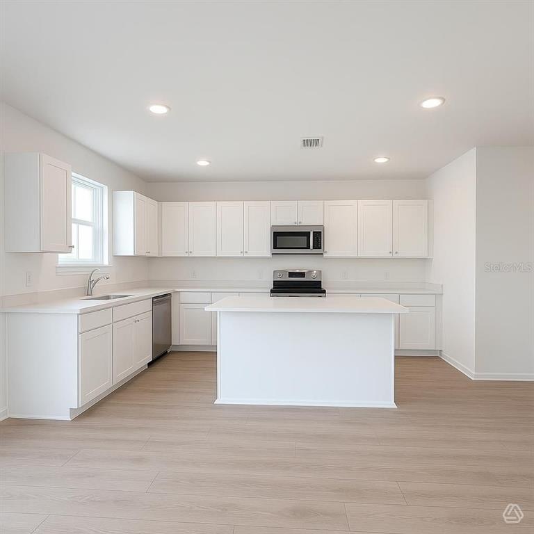 A bright kitchen features white cabinets, stainless steel appliances, a center island, and light flooring — 12923 RED DEER PLACE, PARRISH, FL