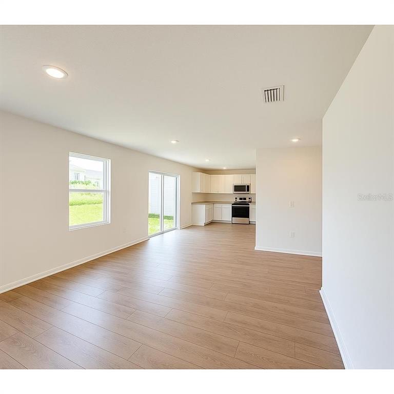 An open-concept living area features light wood-look flooring, recessed lighting, and a kitchen beyond — 12923 RED DEER PLACE, PARRISH, FL