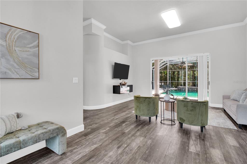 A living room with wood-look flooring, two green armchairs, a wall-mounted television, and a pool view — 4931 TURTLE CREEK TRAIL, OLDSMAR, FL