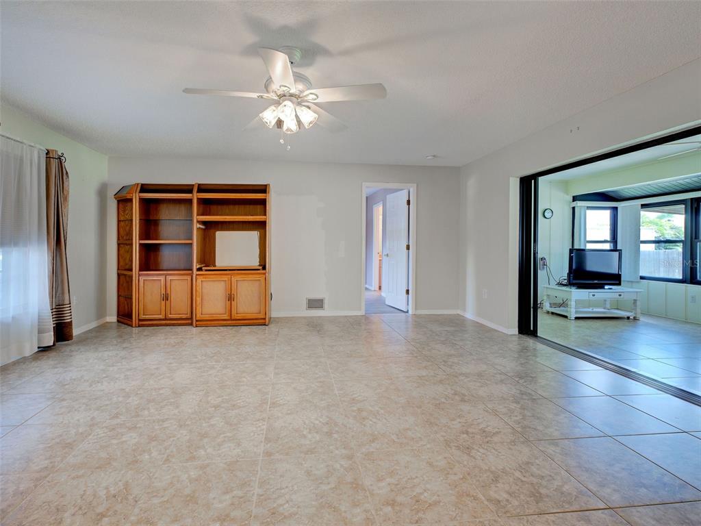 A living room with tile flooring, a ceiling fan, a wooden cabinet, and sliding glass doors — 11081 MAGDALENA AVENUE, ENGLEWOOD, FL