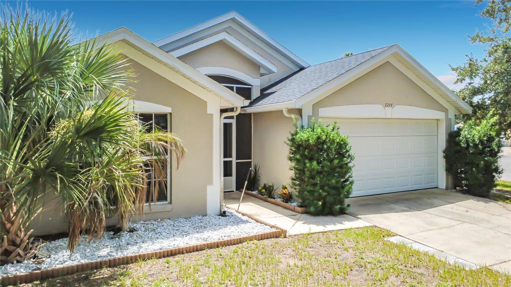 A single-story house with a beige stucco exterior, a two-car garage, and a palm tree — 2244 MALLORY CIRCLE, HAINES CITY, FL
