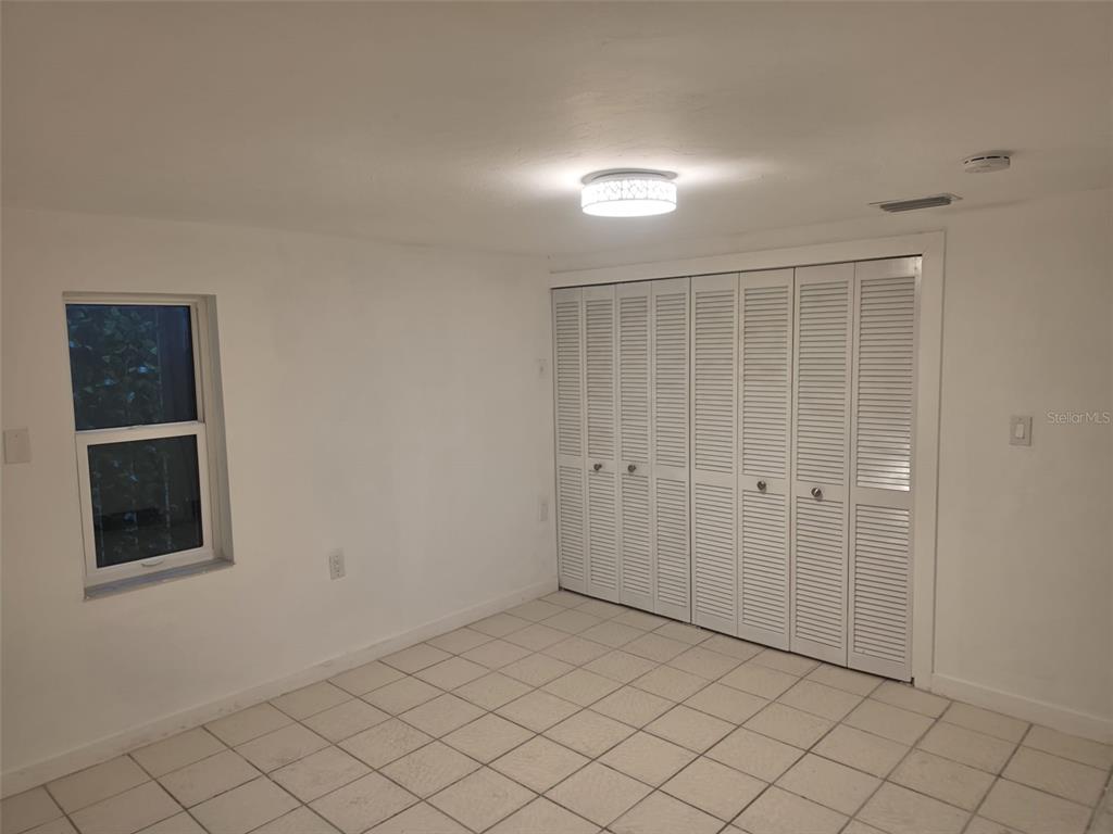 A room with white walls, tiled flooring, a window, and a large louvered closet door — 1844 JOHN RIVERS STREET UNIT B, SARASOTA, FL